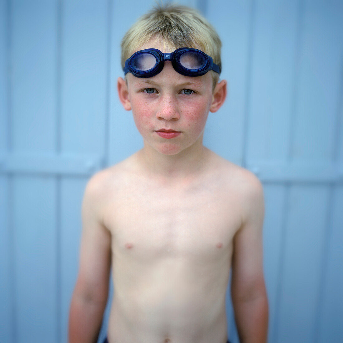Porträt eines Jungen mit Schwimmbrille vor blauer Tafel