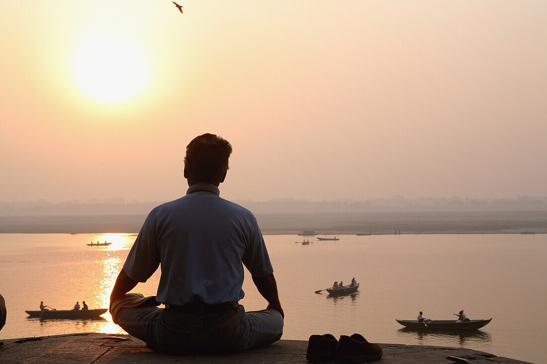 Meditieren / Yoga bei Sonnenaufgang mit Blick auf den Fluss Ganges. Die Kultur von Varanasi ist eng mit dem Fluss Ganges und dessen religiöser Bedeutung verbunden: Sie ist die "religiöse Hauptstadt Indiens" und ein wichtiges Pilgerziel.