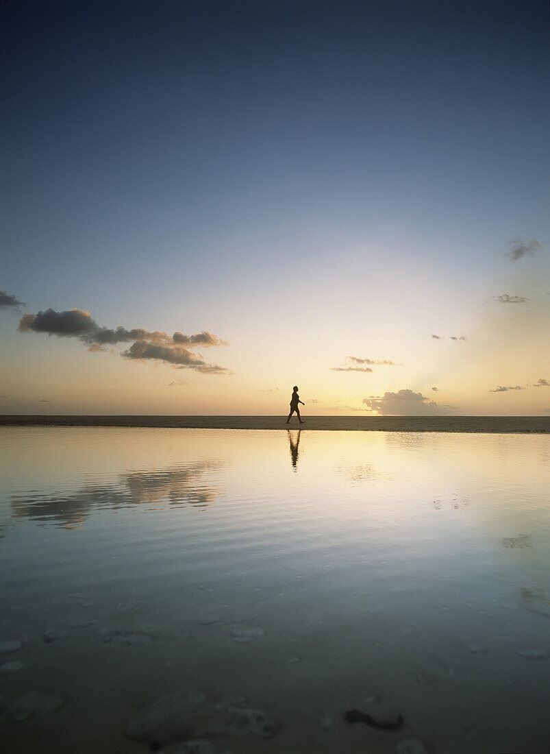 Woman Walking Past Shallow Pool Beside Brighton Beach On West Coast Of Barbados At Dusk.