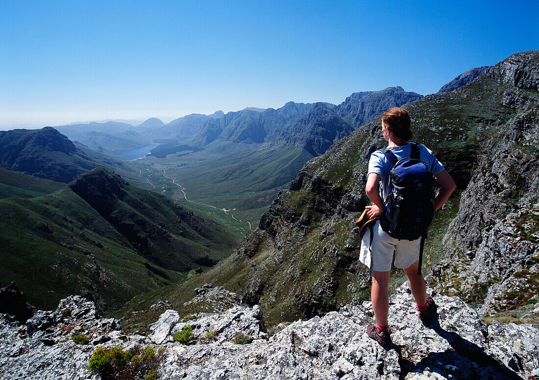 Ein Mann mit einem Rucksack steht auf einem Bergrücken und blickt über das Tal und die Bergkette hinaus