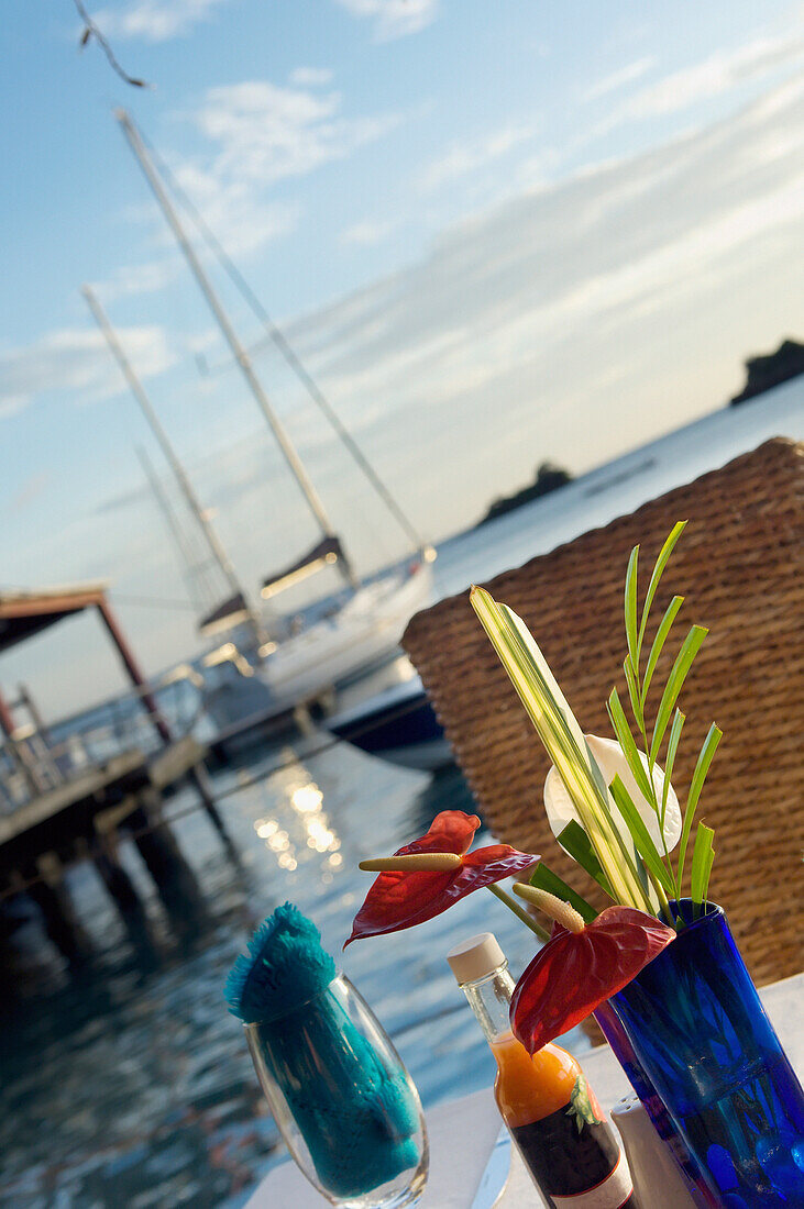 Im Freien gedeckte Tische im Dodgy Dock Restaurant und Lounge Bar in der Nähe des Ozeans mit Segelbooten dahinter. Blaue Vase mit Blumen, Weinglas; Grenada, Karibik