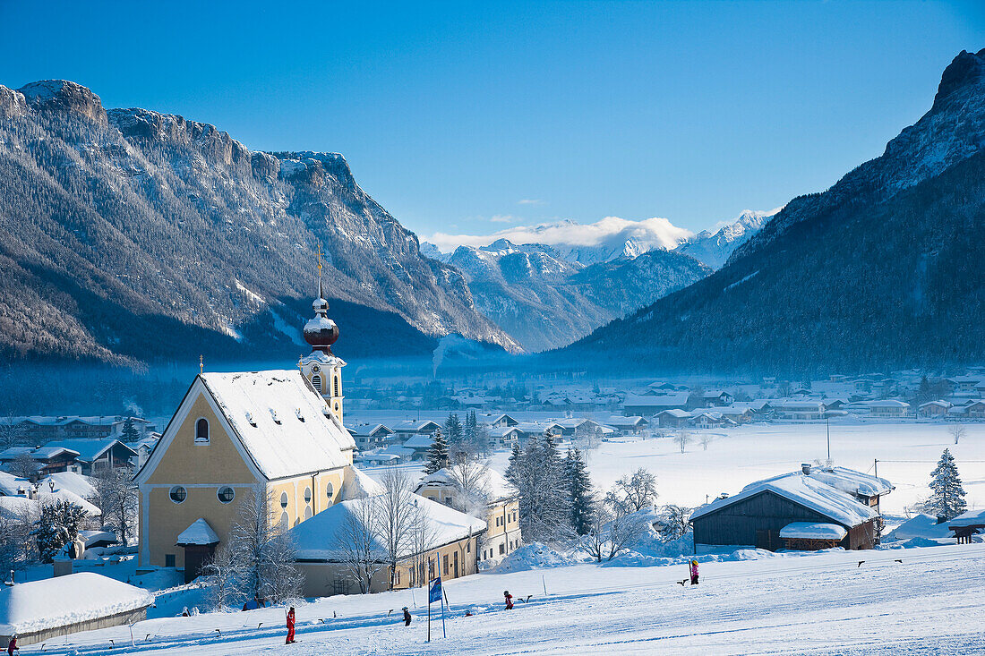 Schneebedeckte Alpenlandschaft mit Bergen, malerische Kirche, Ski- und Snowboardgebiet in Waidring, Österreichische Alpen, Österreich