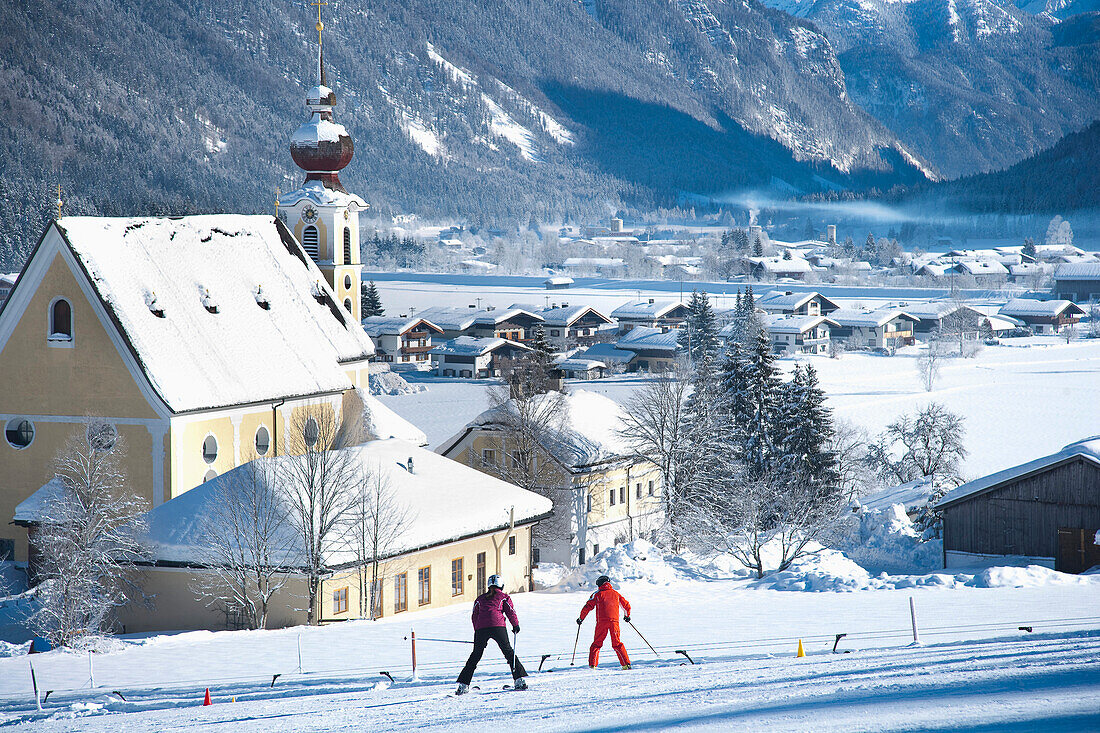 Schneebedecktes Dorf mit Bergen und malerischer Kirche in einem Tal unterhalb der Skipisten in Waidring, Österreichische Alpen, Österreich