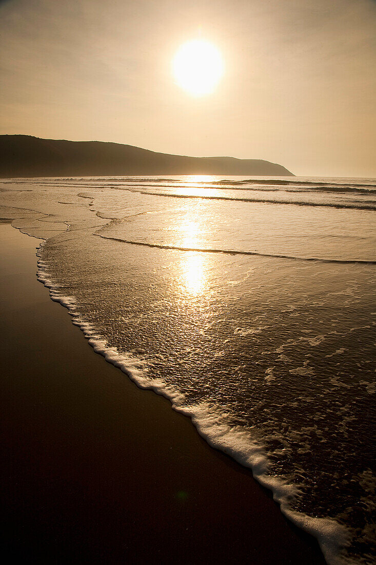 Wellenplätschern am Ufer bei Sonnenuntergang in Putsborough Sands, Nord-Devon, Großbritannien