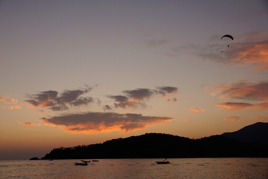 Gleitschirmflieger bei Sonnenuntergang im Sinkflug über Oludeniz an der Türkis-Küste, Südtürkei