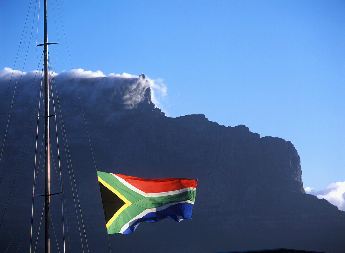Südafrikanische Flagge weht über der Victoria and Albert Waterfront mit Kapstadt und dem Tafelberg dahinter, Südafrika.