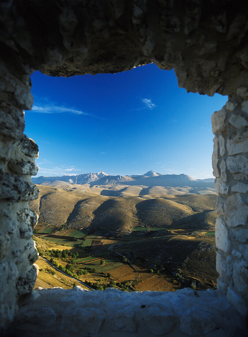 Blick aus einem alten Fenster in einer Gebäuderuine neben der Rocca Calascio auf den Campo Imperatore und den Parco Nazionale Gran Sasso in der Morgendämmerung, Abruzzen, Italien.