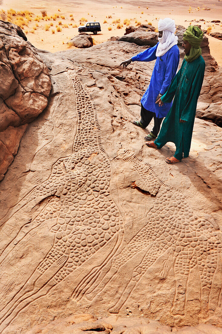 Niger, Sahara-Wüste, Region Agadez, zwei Tuareg-Männer bei der Untersuchung der berühmten Felsgravuren der beiden Riesengiraffen von Dabous, die mindestens 6.000 Jahre alt sein sollen (aus der Zeit der Chasseur Primitif oder der Primitiven Jäger); Dabous