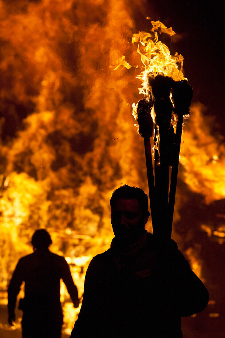 Silhouetten von Menschen, die sich darauf vorbereiten, brennende Fackeln auf ein großes Lagerfeuer in der Barcombe Bonfire Night zu werfen, Barcombe, East Sussex, Großbritannien