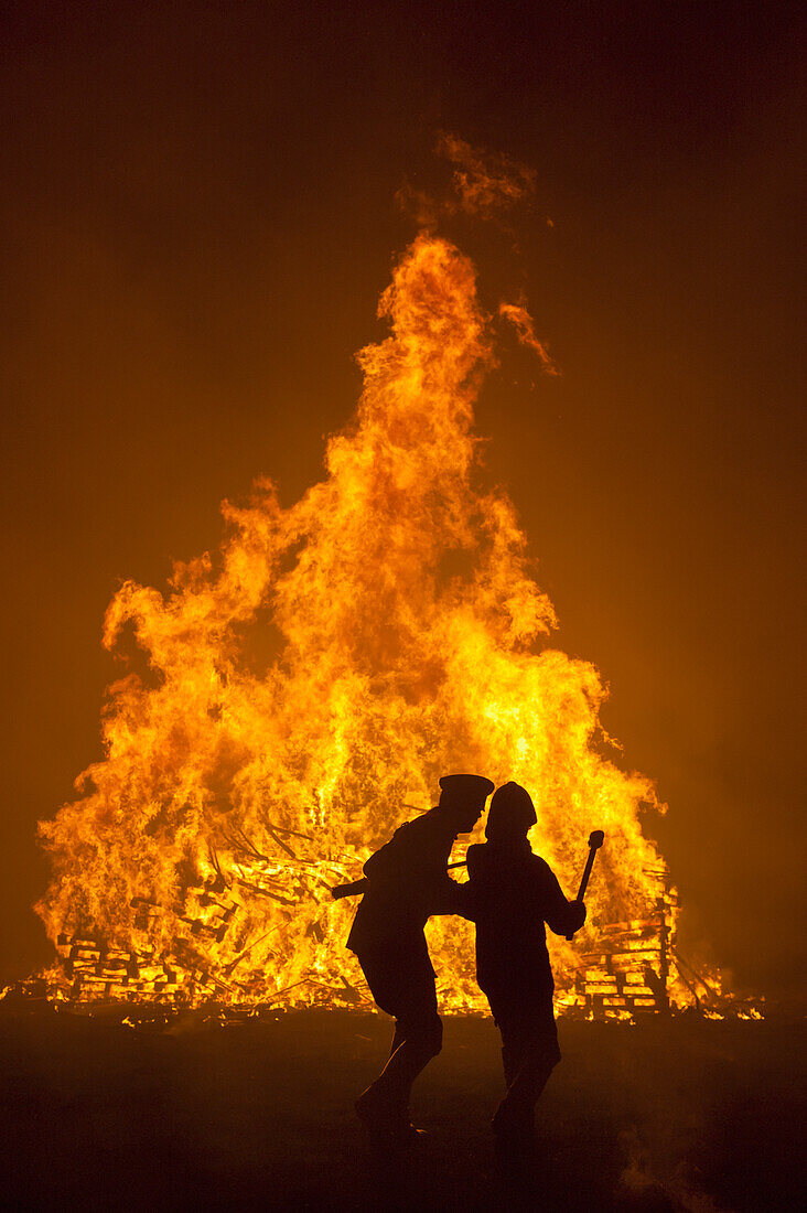Silhouette Of Man Teaching His Son How To Throw Burning Torches On To Large Bonfire At Barcombe Bonfire Night, Barcombe, East Sussex, Uk