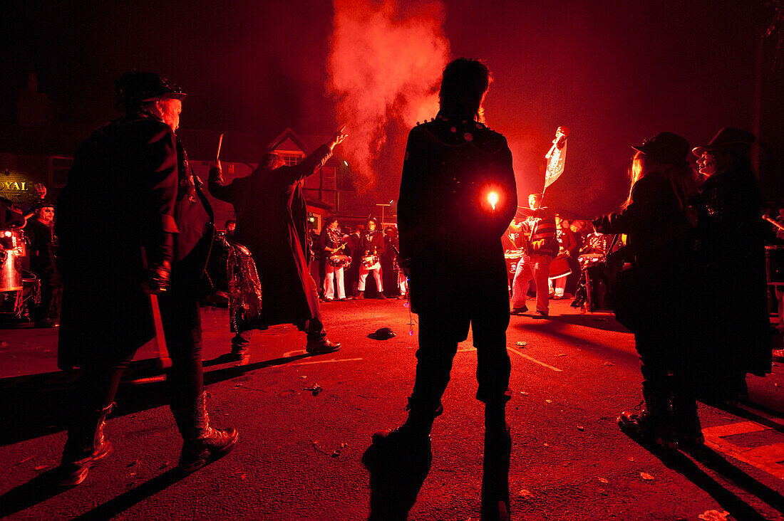 Trommelnde Band im Kreis beleuchtet von roten Fackeln vor dem Pub, Barcombe Bonfire Night, East Sussex, Großbritannien