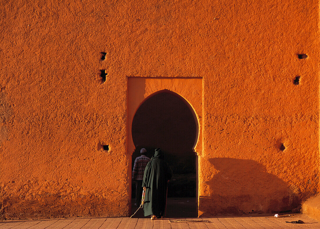 Mann in traditioneller Djelleba, der durch eine kleine Türöffnung in der Stadtmauer von Marrakesch, Marokko, geht.