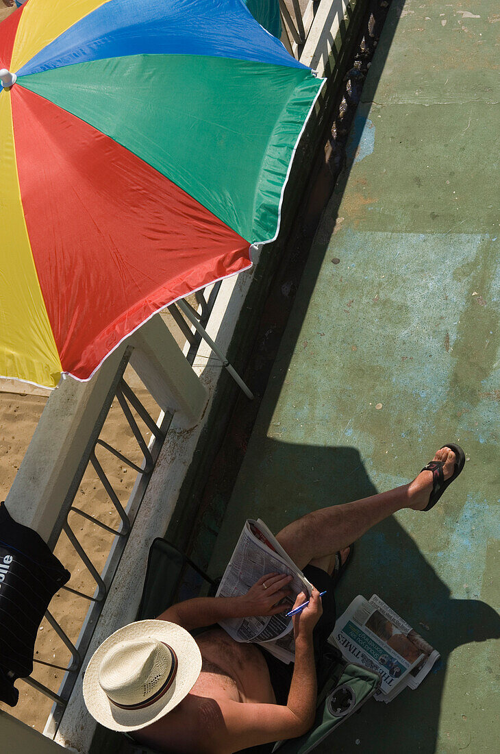 Ein Mann sitzt an der Strandpromenade und liest an einem sonnigen Tag die Zeitungen. Broadstairs, Kent. England. Uk. Foto