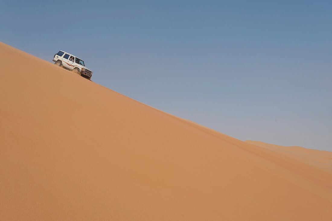 VAE, Abu Dhabi, Geländewagen fährt steile Sanddüne hinunter; Liwa