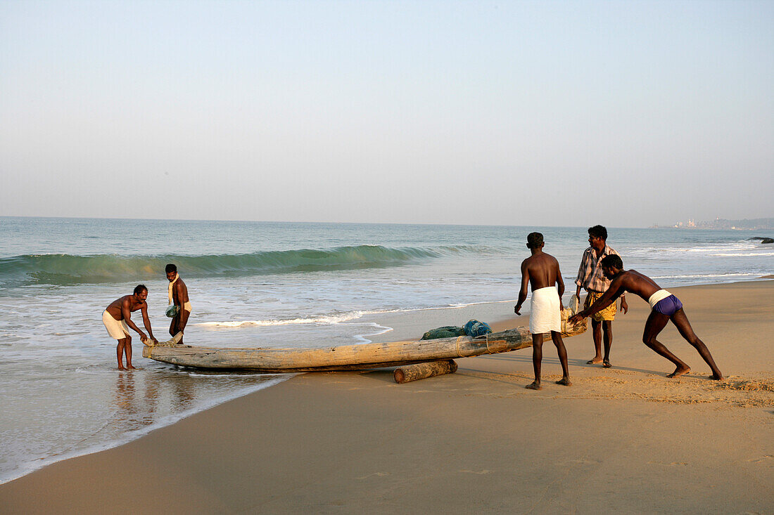 Fischer schieben ihr Boot vom Strand ins Wasser; Kovalam, Kerala, Indien