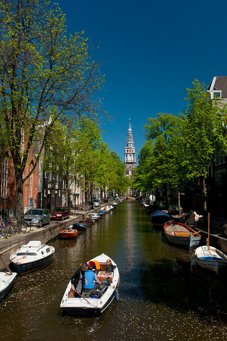 Holland, Menschen in kleinem Boot fahren entlang einer kleinen Gracht mit dem Kirchturm der Zuiderkerk dahinter; Amsterdam