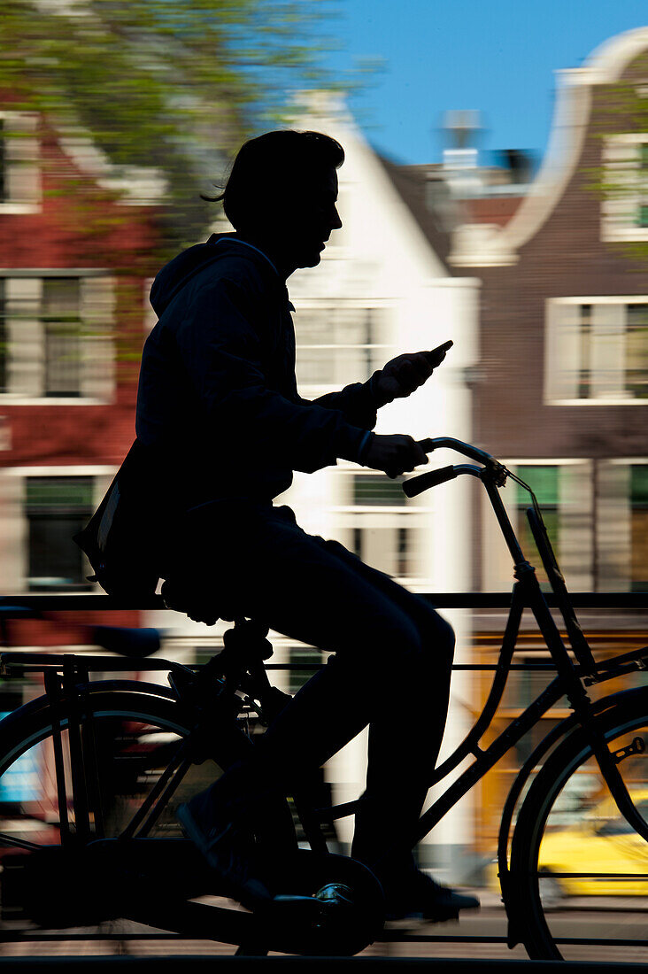 Silhouette eines Radfahrers, der an einer Gracht und Giebelhäusern vorbeifährt,Amsterdam, Holland.