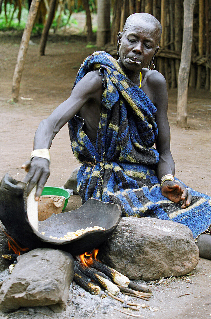 A Mursi tribal woman cooking 'tila' (a traditional dish made with maize or sorghum. Makki /South Omo / Southern Nations, Nationalities & People's Region (Ethiopia).