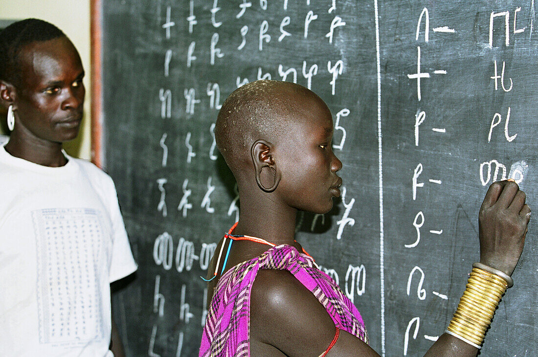 Mursi tribal teacher & pupil during a Mursi Language lesson (written with Amharic Alphabet) in a school run by Christian missionaries (Serving in Mission). Makki / South Omo / Southern Nations, Nationalities & People's Region (Ethiopia).