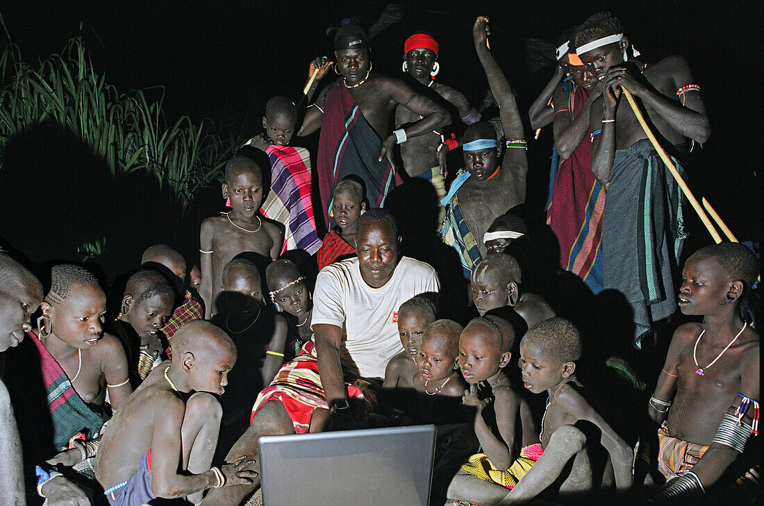 Group of Mursi tribal people looking in owe at the first Mursi owned laptop computer being operated in the deep of night. Makki / South Omo / Southern Nations, Nationalities & People's Region (Ethiopia).