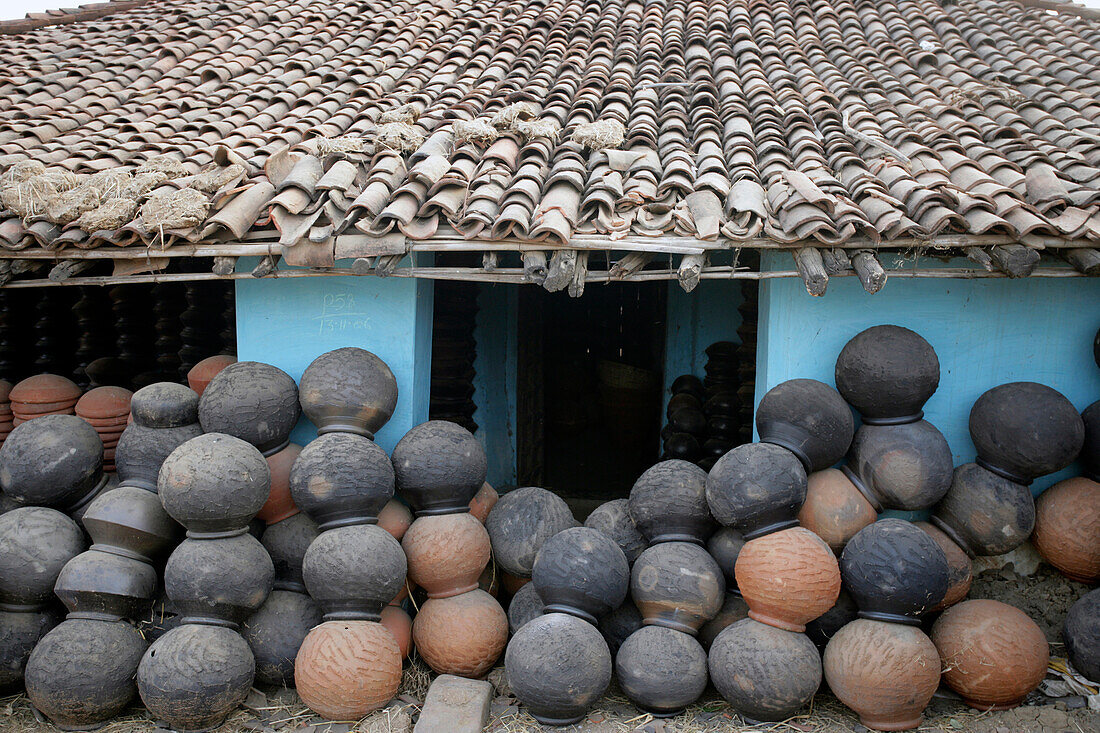 Zahlreiche Keramiktöpfe vor einem blauen Haus gestapelt, Töpferdorf; Madhya Pradesh, Indien
