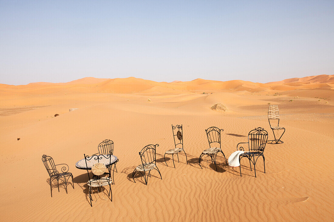 Dining furniture is scattered in desert sands.; Erg Chebbi , Sahara Desert , Morocco