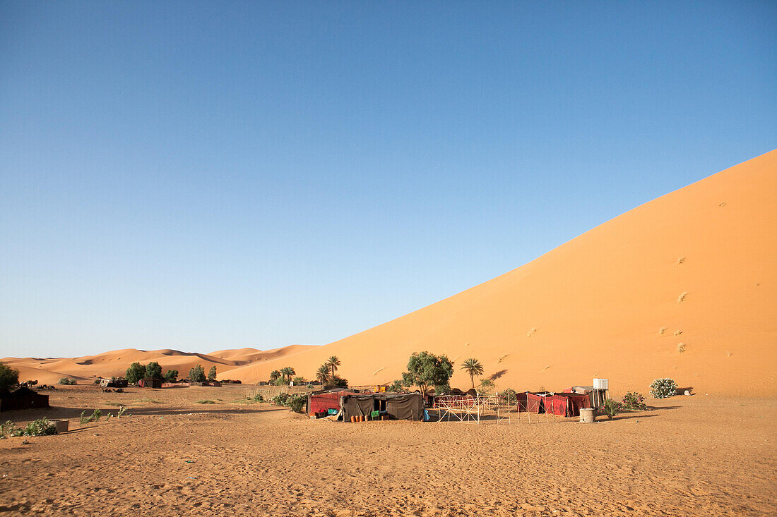 A small tented camp is visible near a sand dune in the Sahara desert.; Erg Chebbi , Sahara Desert , Morocco