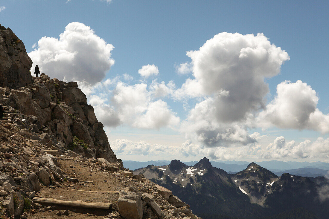 A hiker follows a trail on Mount Rainier with the Cascade Mountain range in the background.; Mount Rainier National Park, Washington