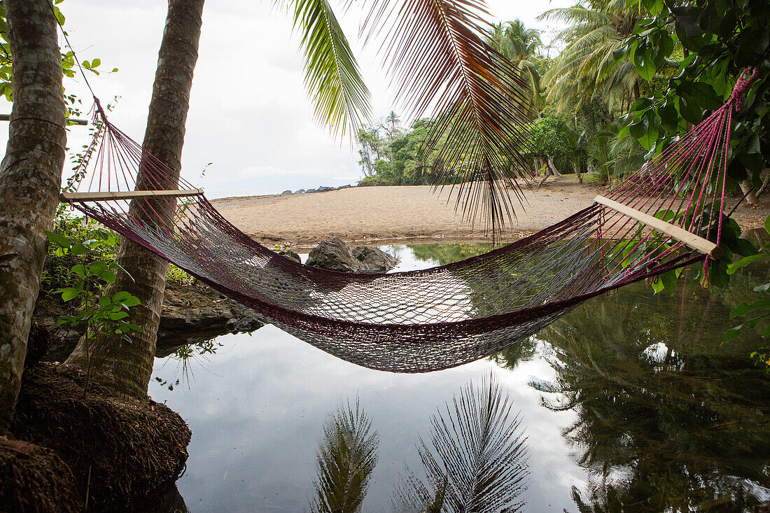 A colorful hammock hangs between two trees and above a river in Caletas Reserve, Osa Peninsula.; Costa Rica