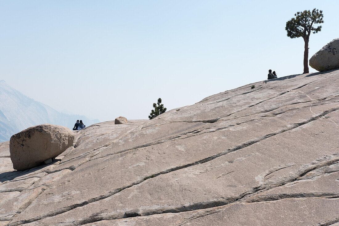 At Olmstead Point, smoke from a wildfire clouds the view of Yosemite National Park as couples sit.; Yosemite National Park, California, United States of America
