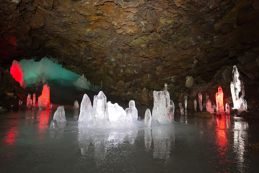 In a cave, stalagmites made of ice are illuminated by light.; Iceland