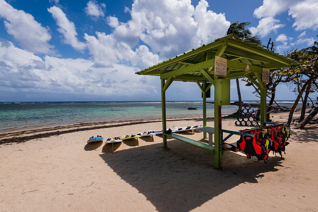 Pavillon mit Schwimmwesten und Wasserbrettern zum Ausleihen am Sandstrand Plage de la Caravelle am Ufer des Karibischen Meeres, Sainte-Anne auf Grande-Terre; Guadeloupe, Französische Westindische Inseln