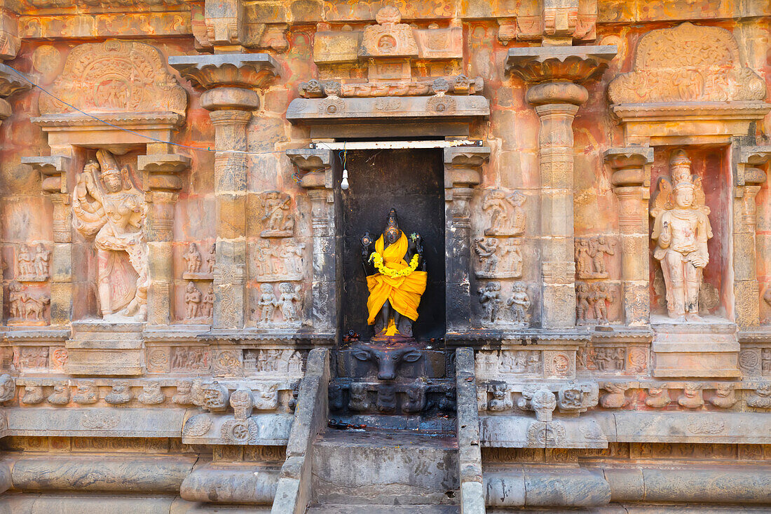Nische mit einer in leuchtend gelbe Seide gehüllten Hindu-Gottheit in der Steinwand des Airavatesvara-Tempels aus der dravidischen Chola-Zeit; Darasuram, Tamil Nadu, Indien