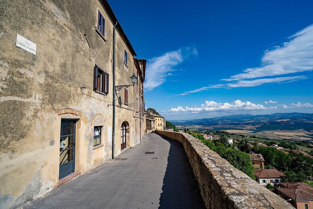 Mittelalterliche Gebäude und Steinmauern säumen die Allee mit Blick auf die Landschaft in der historischen Altstadt von Volterra; Volterra, Toskana, Italien