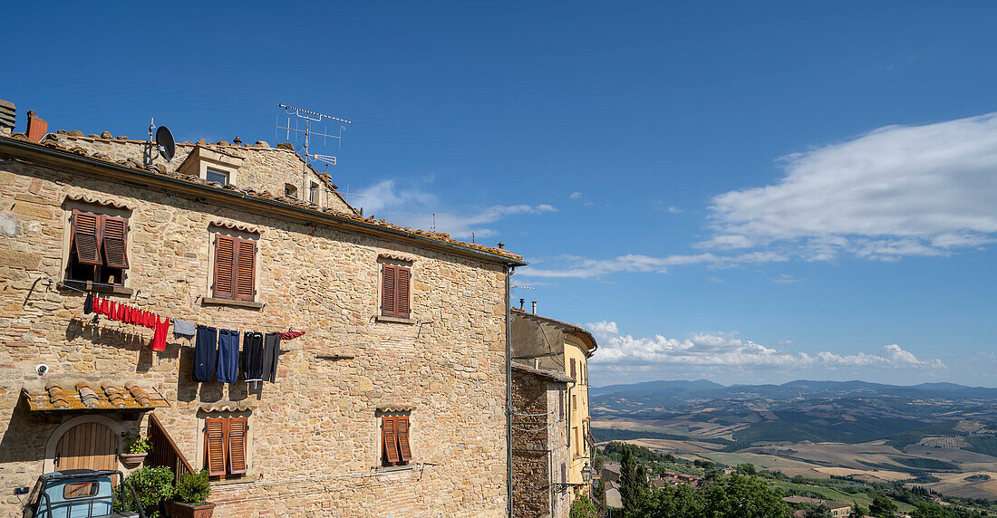 Wäsche, die zum Trocknen an der Seite eines mittelalterlichen Gebäudes in der historischen Altstadt von Volterra aufgehängt wird, mit einem Blick auf die Landschaft im Hintergrund; Volterra, Toskana, Italien