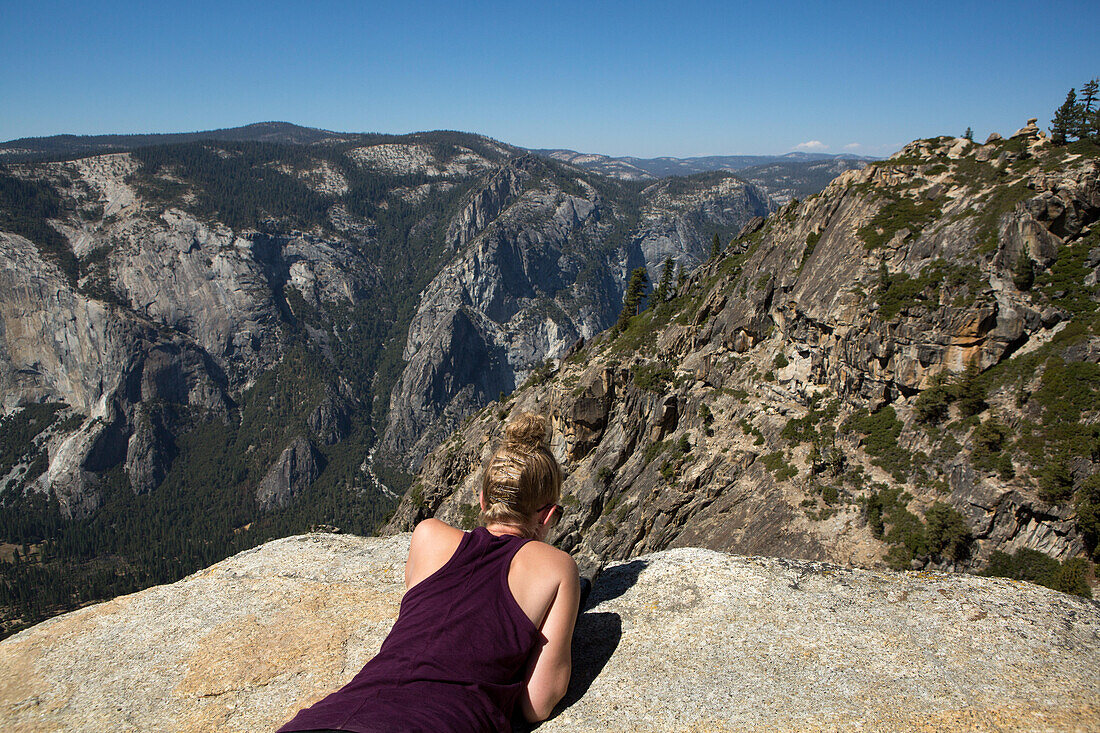 At the Taft Point hiking trail peak, a hiker looks over the edge to Yosemite Valley below.; Yosemite National Park, California