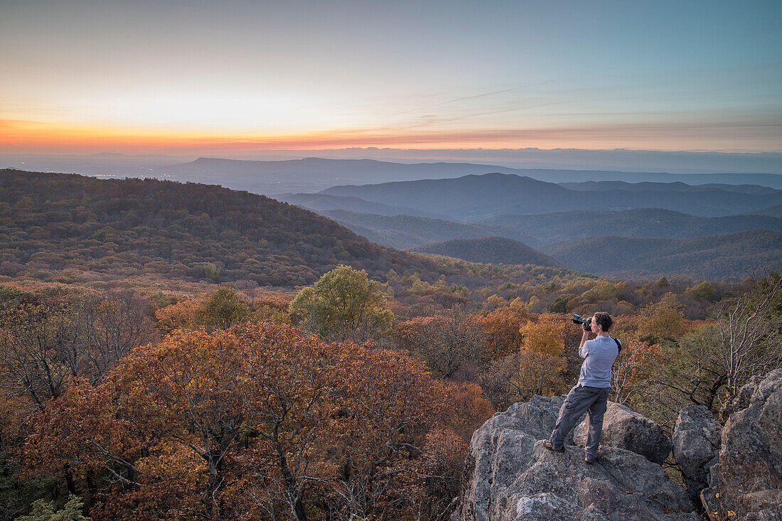 A man takes a photo at sunset in fall at Bearfence Mountain in Shenandoah National Park, Virginia.