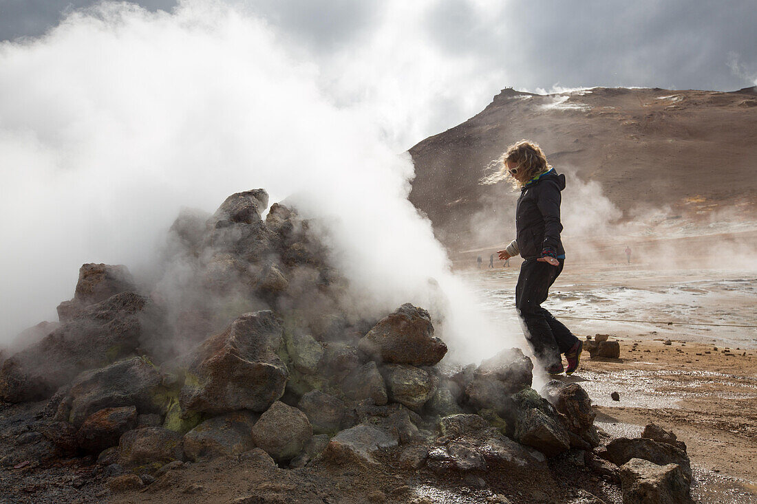 A woman walks among the steaming mud pots geothermal area near Lake Myvatn.; Iceland