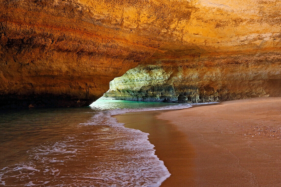 Sandstone rock formations, sea arch along the ocean coast of the Algarve with surf and sandy beach at low tide; Algarve, Lagoa, Iberian Peninsula, Portugal