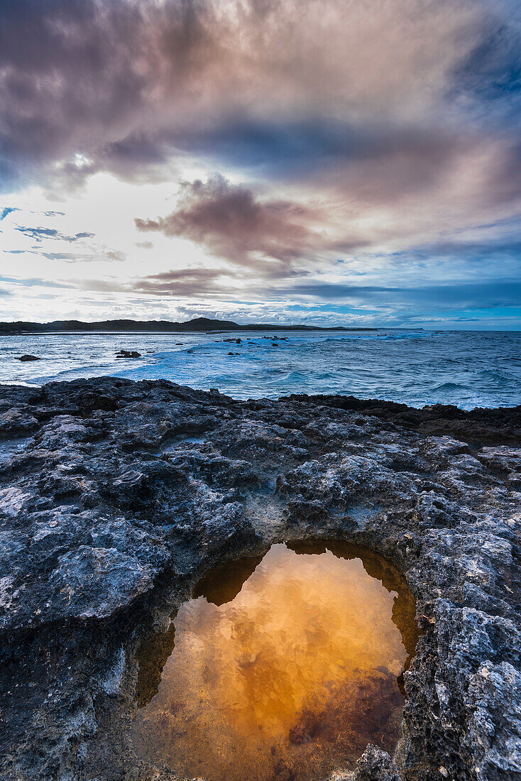 Volcanic rock formations and golden light reflected in a tidal pool on the beach at Pointe des Chateaux under a cloudy sky; Grande-Terre, Guadeloupe, French West Indies