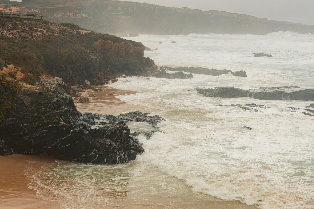 Nebel über dem Strand und der zerklüfteten Küstenlinie des Praia do Malhao; Alentejo, Portugal