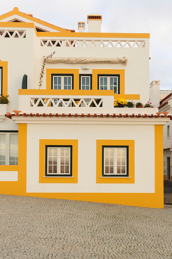 Außenansicht eines hell gestrichenen Hauses an einer schrägen Kopfsteinpflasterstraße; Zambujeira do Mar, Alentejo, Portugal