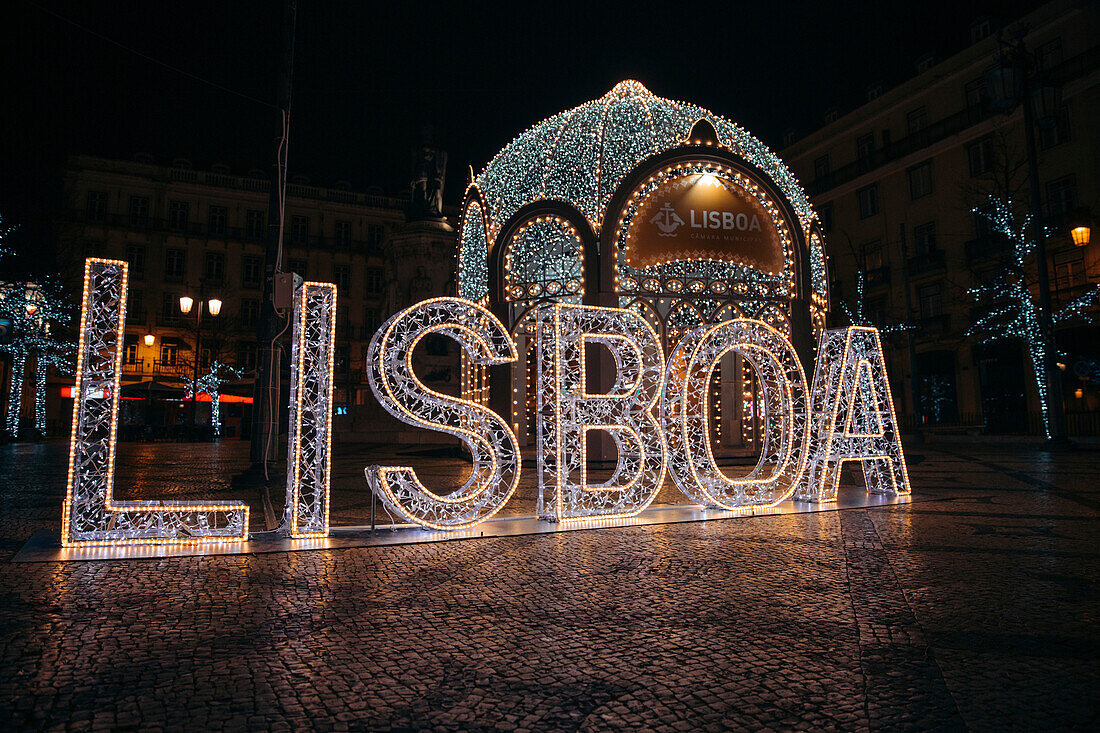 Weihnachtsbeleuchtung an einem Pavillon mit einem beleuchteten Lisboa-Schild auf einem Stadtplatz in den Stadtteilen Chiado und Bairro Alto; Lissabon, Estremadura, Portugal