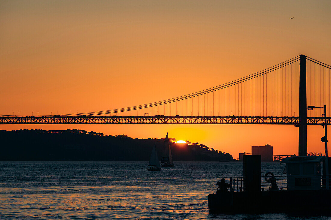 Silhouette der Brücke 25 de Abril über den Tejo, die Lissabon und Almada bei Sonnenuntergang verbindet; Lissabon, Estremadura, Portugal