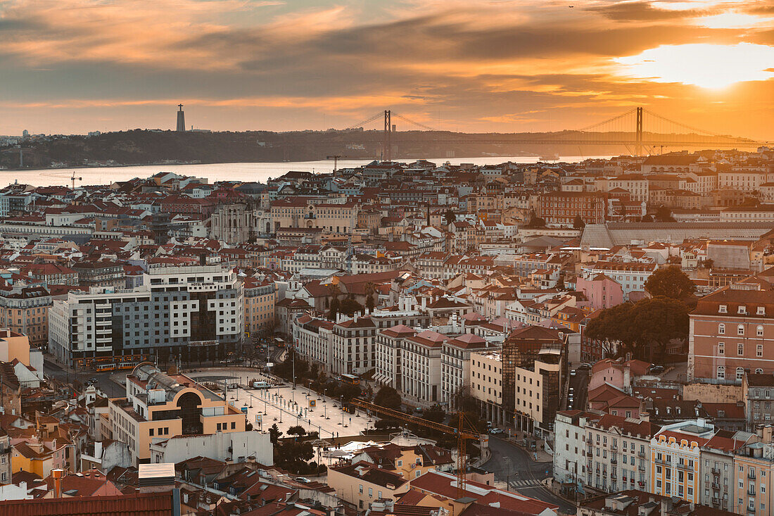 Überblick über die Stadt Lissabon, mit den pastellfarbenen Gebäuden der Altstadt, der Tejo-Mündung und der Hängebrücke Ponte 25 de Abril bei Sonnenuntergang; Lissabon, Portugal
