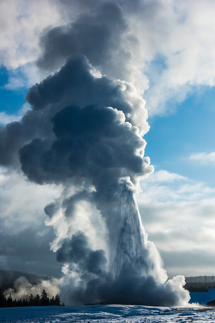 Close-up of Old Faithful erupting with gushing water and large plumes of steam rising into the cloudy blue sky in Upper Geyser Basin, Yellowstone National Park; Wyoming, United States of America