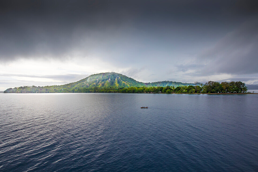 Menschen in einem Kanu vor dem Inseldschungel von Dobu Island, aus dessen Regenwäldern Dampf aufsteigt, auf den D'Entrecasteaux-Inseln, Papua-Neuguinea; Dobu Island, D'Entrecasteaux-Inseln, Papua-Neuguinea