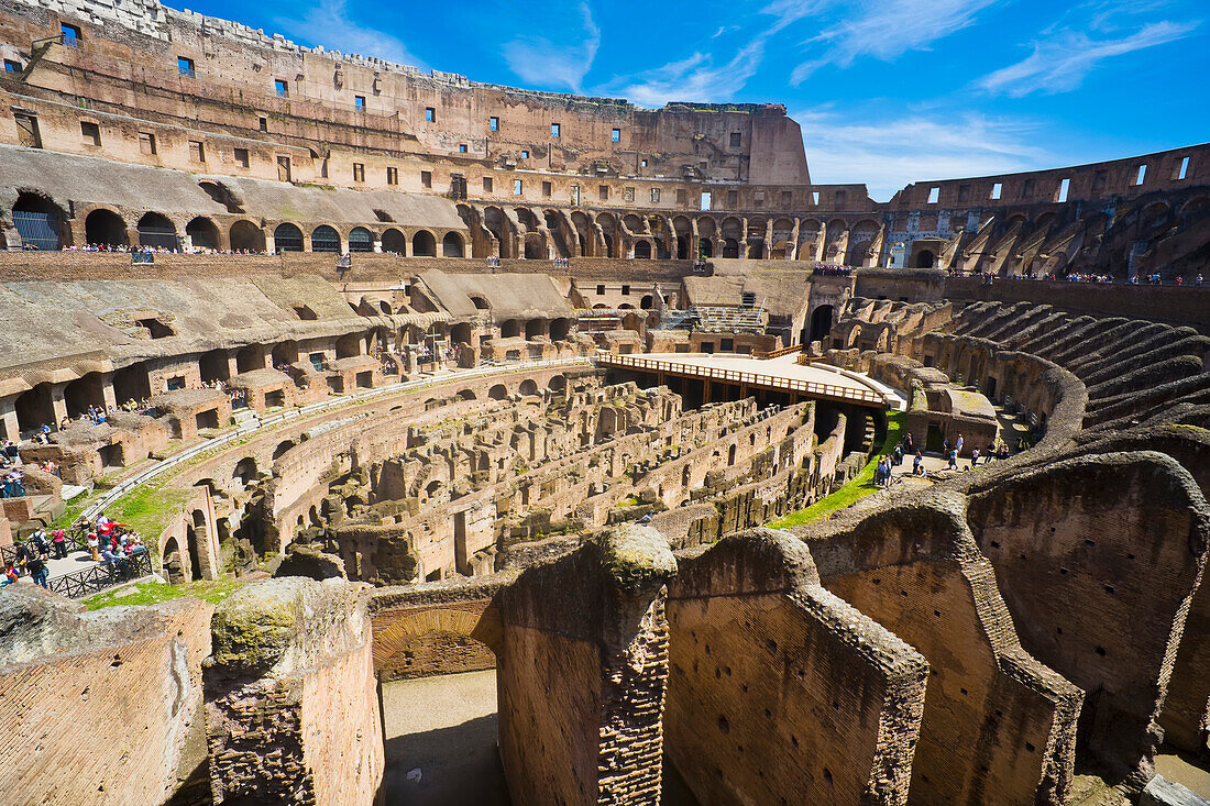 Overview of the interior of the iconic Colosseum against a blue sky with crowds of tourists sightseeing; Rome, Lazio, Italy