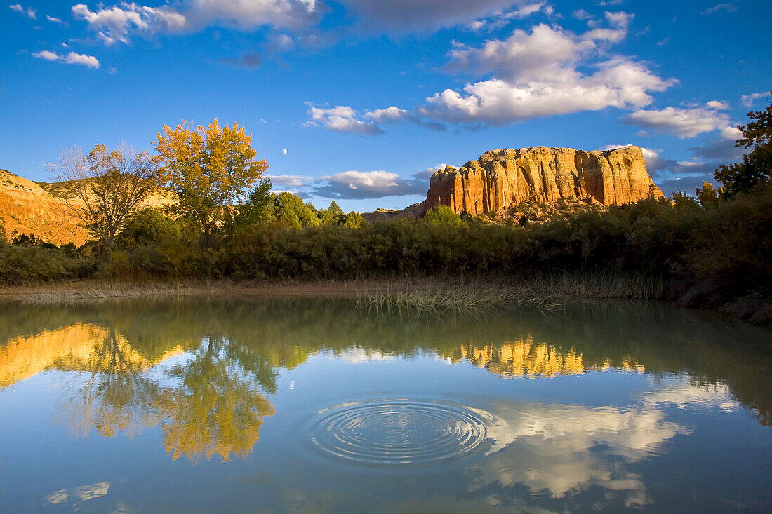 Fall color and rock formations casting reflections in calm water.