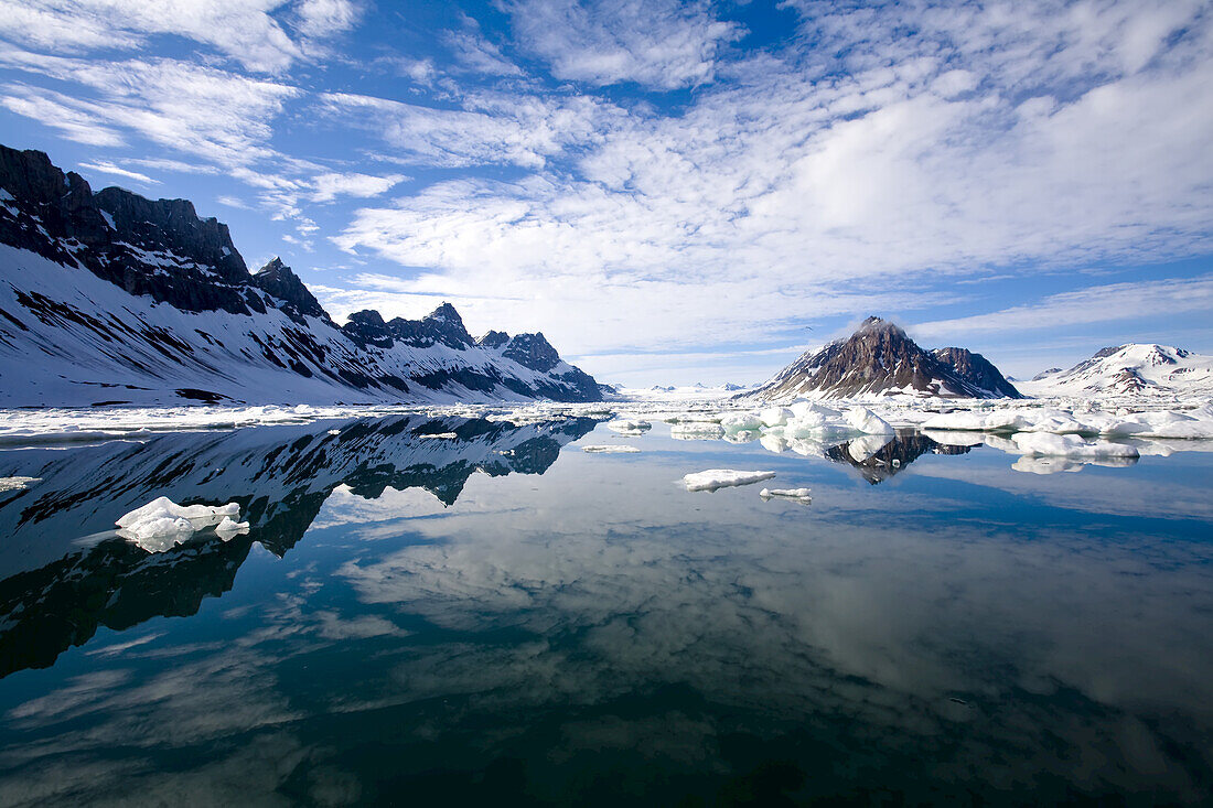 Jagged coastal peaks casting reflections in cold Arctic waters.